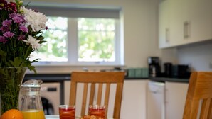 Een ontbijtsetting met een bord croissants, een schaal sinaasappels, een vaas bloemen en twee glazen sinaasappel-sap op een houten tafel.