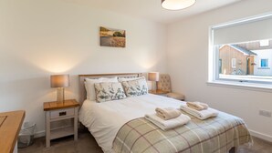 Een slaapkamer met een bed, twee nachtkastjes, een raam en een schilderij aan de muur.