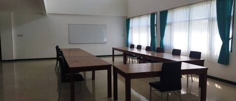 Une salle de conférence avec une longue table et des chaises, un tableau blanc et de grandes fenêtres équipées de rideaux.