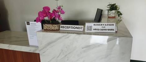 A reception desk with a marble top, a sign for the receptionist, a QR code for reservations, and a potted plant.