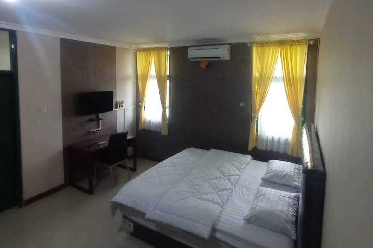 A hotel room with a bed, a desk, a chair, and an air conditioning unit.
