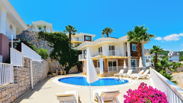 A pool area with lounge chairs and a white umbrella, surrounded by stone walls and palm trees. - Beautiful Detached Villa With Private Pool And Stunning Views,Walkable to Town. (Dalanan)