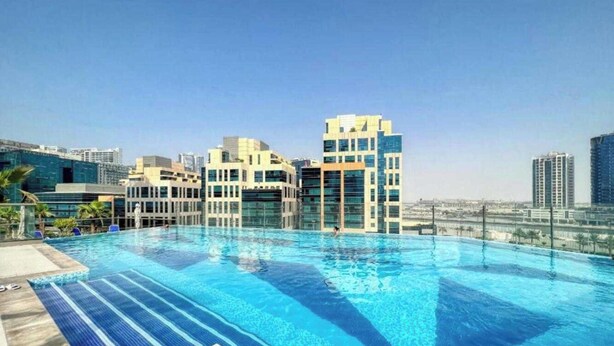 Une piscine sur le toit, avec une eau d’un bleu limpide, entourée de bâtiments modernes et sous un ciel dégagé.