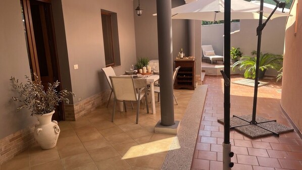 Eine Terrasse mit Esstisch, Stühlen, einem Topfpflanzen und einer Pergola mit Sonnenschirm.
