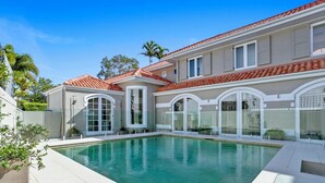 A modern house with a swimming pool, large windows, and a tiled roof. - Elegance On The River, Noosa Waters (Noosaville)