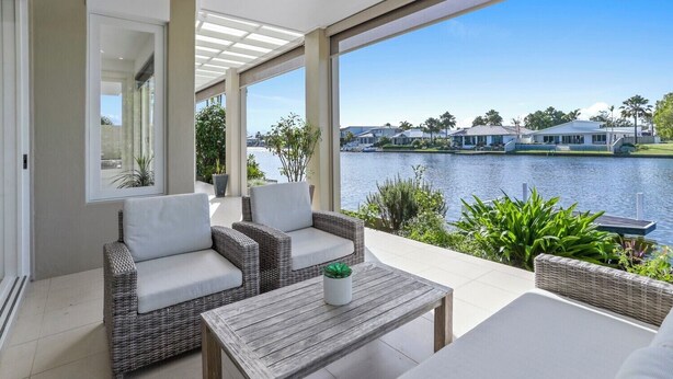 A modern outdoor patio with wicker furniture and a view of a lake and houses. - Elegance On The River, Noosa Waters (Noosaville)