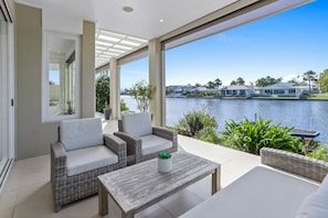 A modern outdoor patio with wicker furniture and a view of a lake and houses. - Elegance On The River, Noosa Waters (Noosaville)