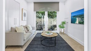 A modern living room with a sofa, coffee table, and a large window with a view of greenery. - Elegance On The River, Noosa Waters (Noosaville)