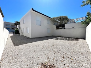 A white building with a gravel courtyard, a staircase, and a tree.