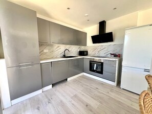 Una cucina moderna con mobili grigi, una cappa aspirante nera, forno integrato e frigorifero bianco.