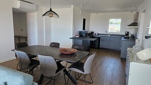A modern kitchen with a dining area, featuring a dark marble table, grey chairs, and a hanging light fixture. - Appartement Neuf de 84 m2 Avec Terrasse de 60 m2 vue mer (L'Île-Rousse)