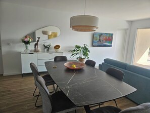 Et moderne spiseområde med et marmorbord, sorte stole, en blå sofa og en hængende lampe.