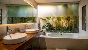 A modern bathroom with two sinks, a bathtub, and a large window with a view of indoor plants.