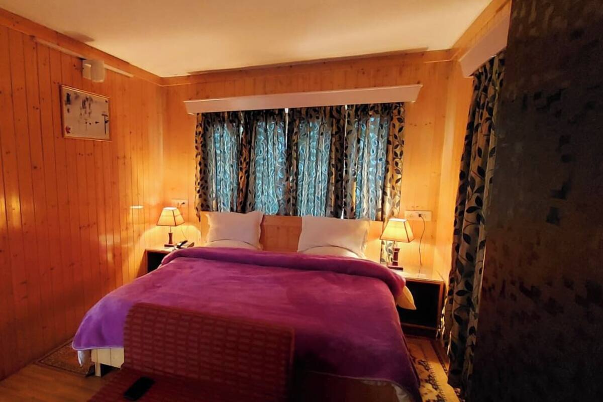 Un dormitorio con paneles de madera, una cama, dos lámparas de noche y un ventanal con cortinas estampadas.