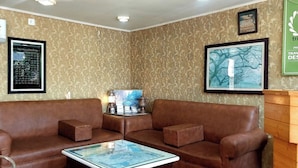 A room with a brown leather sofa, a small table with a map, and framed pictures on the walls. - Ikraam Inn (Srinagar)