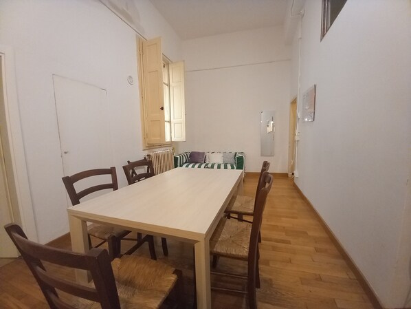 A dining area with a long table and chairs, a radiator, a window with open shutters, and a mirror on the wall. - Cavour 46 First in Firenze (Florence)