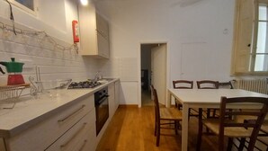 Cozinha compacta com armários brancos, fogão a gás e área de refeições com cadeiras de madeira.