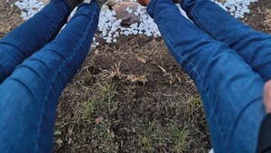 Eine Person sitzt mit verschränkten Beinen vor einem Lagerfeuer, umgeben von weißen Kieselsteinen und Steinen.