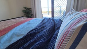 Ein Schlafzimmer mit Bett, einem Fenster mit Vorhängen und Blick ins Freie.