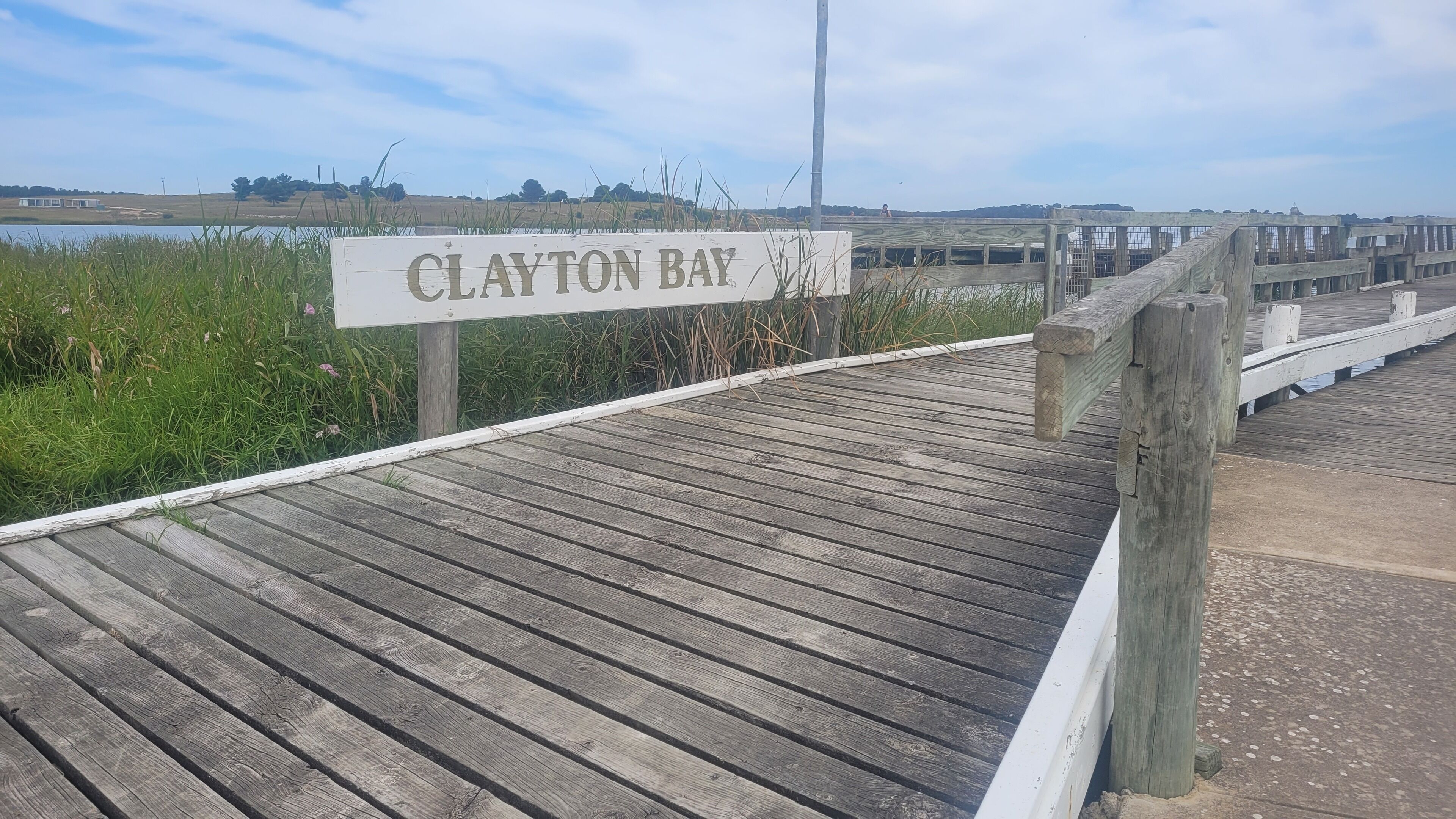 Een houten looppad dat naar Clayton Bay leidt, met een bord.