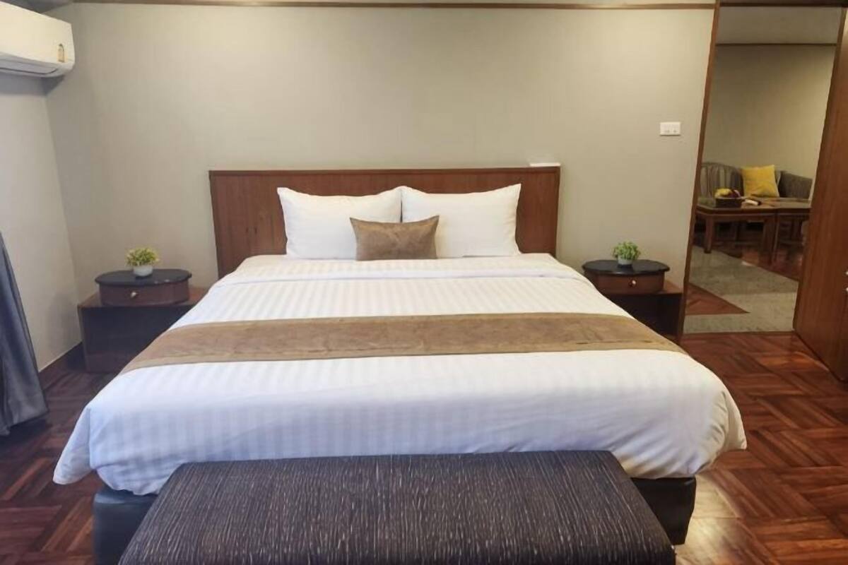 A hotel room with a large bed, two bedside tables with lamps, a bench at the foot of the bed, and a mirror on the wall.