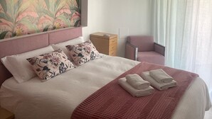 A neatly made bed with a red blanket and pillows, a ceiling fan, a nightstand, a wooden cabinet, and a window with sheer curtains. - Enjoying the beach (Playa de Gandia)