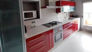 A modern kitchen with white and red cabinetry, a built-in microwave, a gas stove, and a large window providing natural light. - Enjoying the beach (Playa de Gandia)