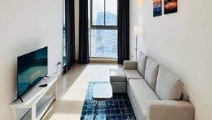 A modern living room with a sofa, a TV, a coffee table, and a view of a cityscape through large windows. - OYO 1194 Home Orion Building 514 (Dubai)