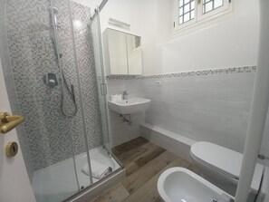 Une salle de bain avec une douche à parois de verre, un lavabo blanc, des toilettes et un plancher en bois.