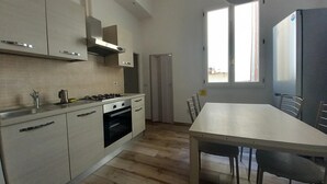 A modern kitchen with white cabinets, a stove, and an oven. There is a dining table with chairs and a window with a view of the outside. - Cavour 46 Second in Firenze (Florence)