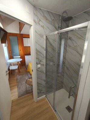 A modern bathroom with a glass-enclosed shower, marble walls, and a wooden floor. - Casa da Capela (Folgosa)