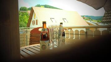 A balcony with two bottles and a glass, overlooking a house with a tiled roof and a fence.