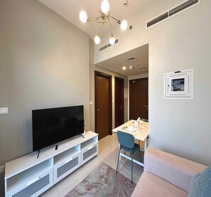 A modern living room with a flat-screen TV on a white entertainment unit, a dining table with chairs, and a sofa. - OYO 1206 Home Fully Furnished 1-Bed Apartment At Arjan Orion Building (Dubai)