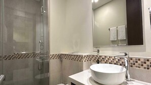 Une salle de bain moderne avec une douche à parois de verre, des toilettes blanches et un grand lavabo surmonté d’un miroir.