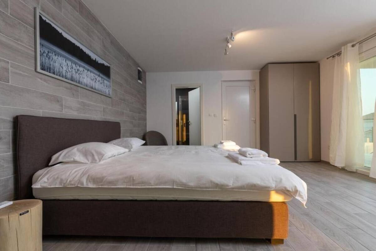 A modern bedroom with a large bed, a grey headboard, and a wooden floor.