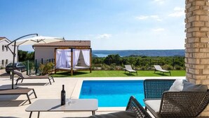 Uma área na piscina com espreguiçadeiras, um pequeno gazebo e vista para o mar.