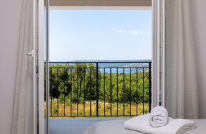 A room with a bed, a window with curtains, and a view of greenery and a body of water. - Diminici Villas (Rasa)