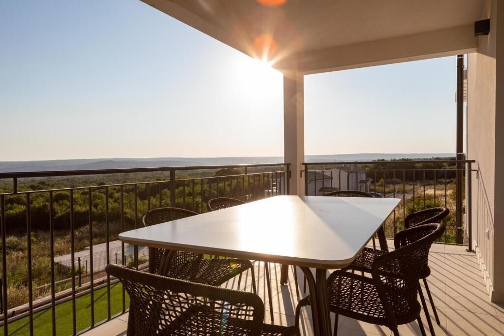 Un balcon avec une table et des chaises, offrant une vue sur un paysage verdoyant et des collines lointaines.