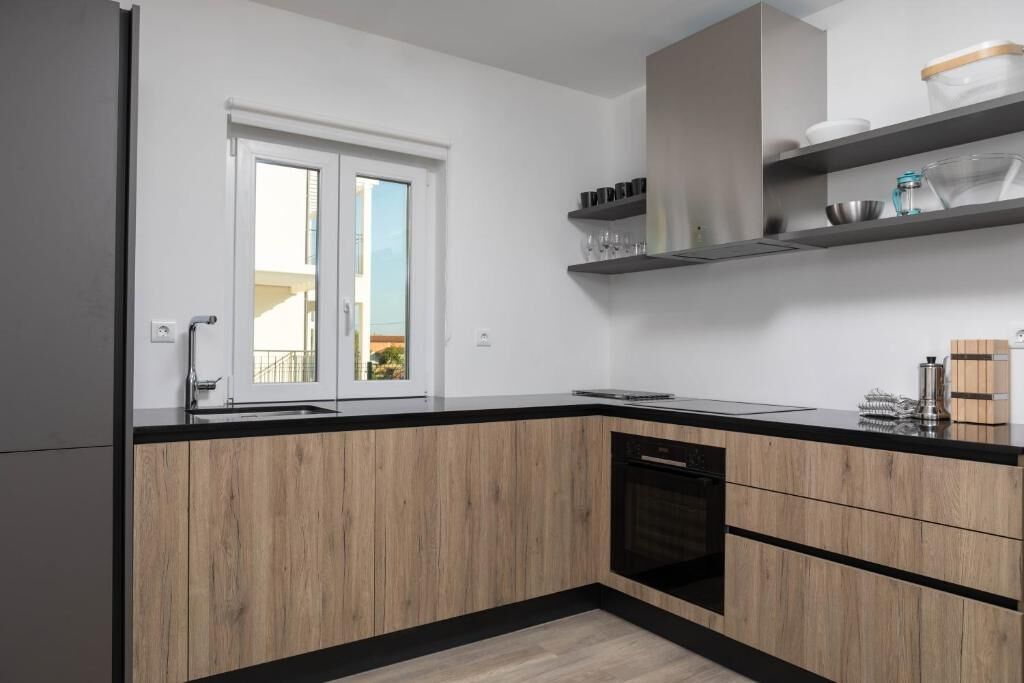 A modern kitchen with wooden cabinets, black countertops, and built-in shelves above the counter.
