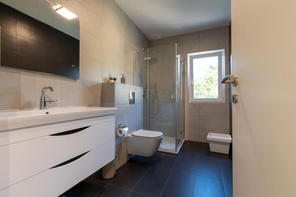 A modern bathroom with a white vanity, a glass shower enclosure, and a toilet.