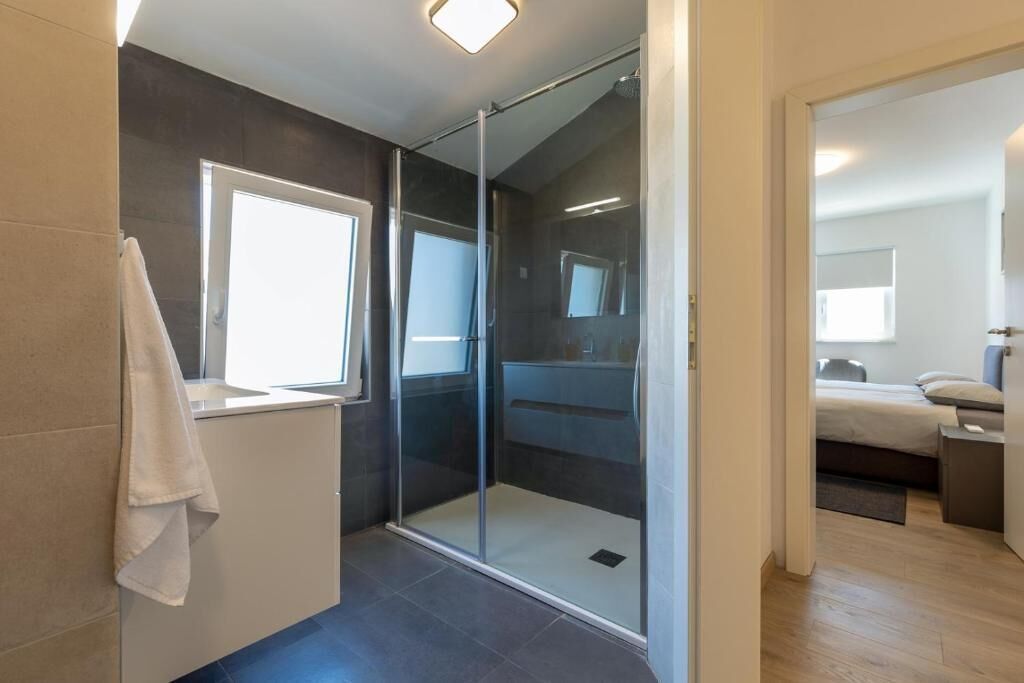 A modern bathroom with a glass shower enclosure, a towel rack, and a window.