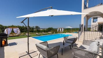 Relax by the pool surrounded by a patio with wicker chairs and a table.