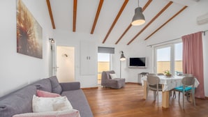 A modern living room with a grey sofa, a dining table with chairs, a TV, and a balcony with a pink curtain. - Apartments Tara & Noemi (Rovinj)
