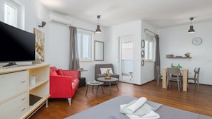 A modern living room with a flat-screen TV, red sofa, grey couch, and a grey sofa bed. There is a small round table with a plant, a dining table with chairs, and a clock on the wall. - Apartments Tara & Noemi (Rovinj)