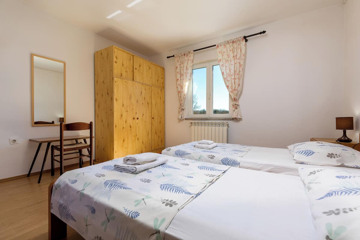 Une chambre avec deux lits, une armoire en bois, un bureau et une fenêtre avec des rideaux.