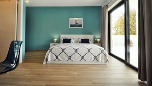 Quarto com cama, cadeira, mesa de cabeceira e janela com cortinas.