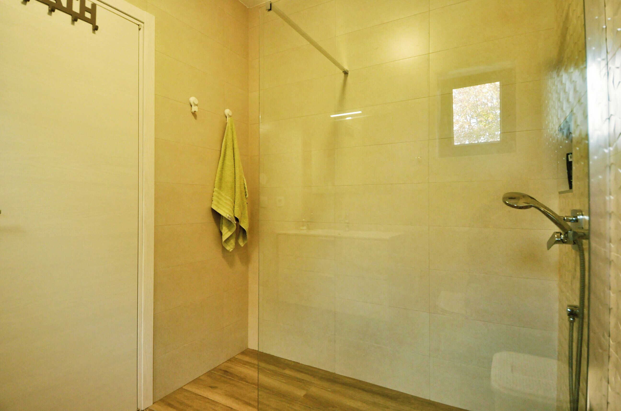 Une douche fermée par des parois de verre, dotée d’un pommeau de douche à main, d’un porte-serviettes avec une serviette verte et d’un plancher en bois.