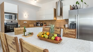A modern kitchen with white cabinets, stainless steel appliances, and a wooden dining table with a fruit bowl. - House Kaliope (Zadar)