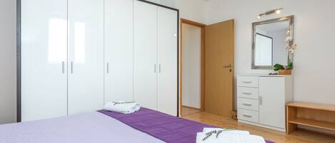 Ein Schlafzimmer mit einem großen Bett, einem Kleiderschrank, einem Schminktisch mit Spiegel und einer Holzbank.