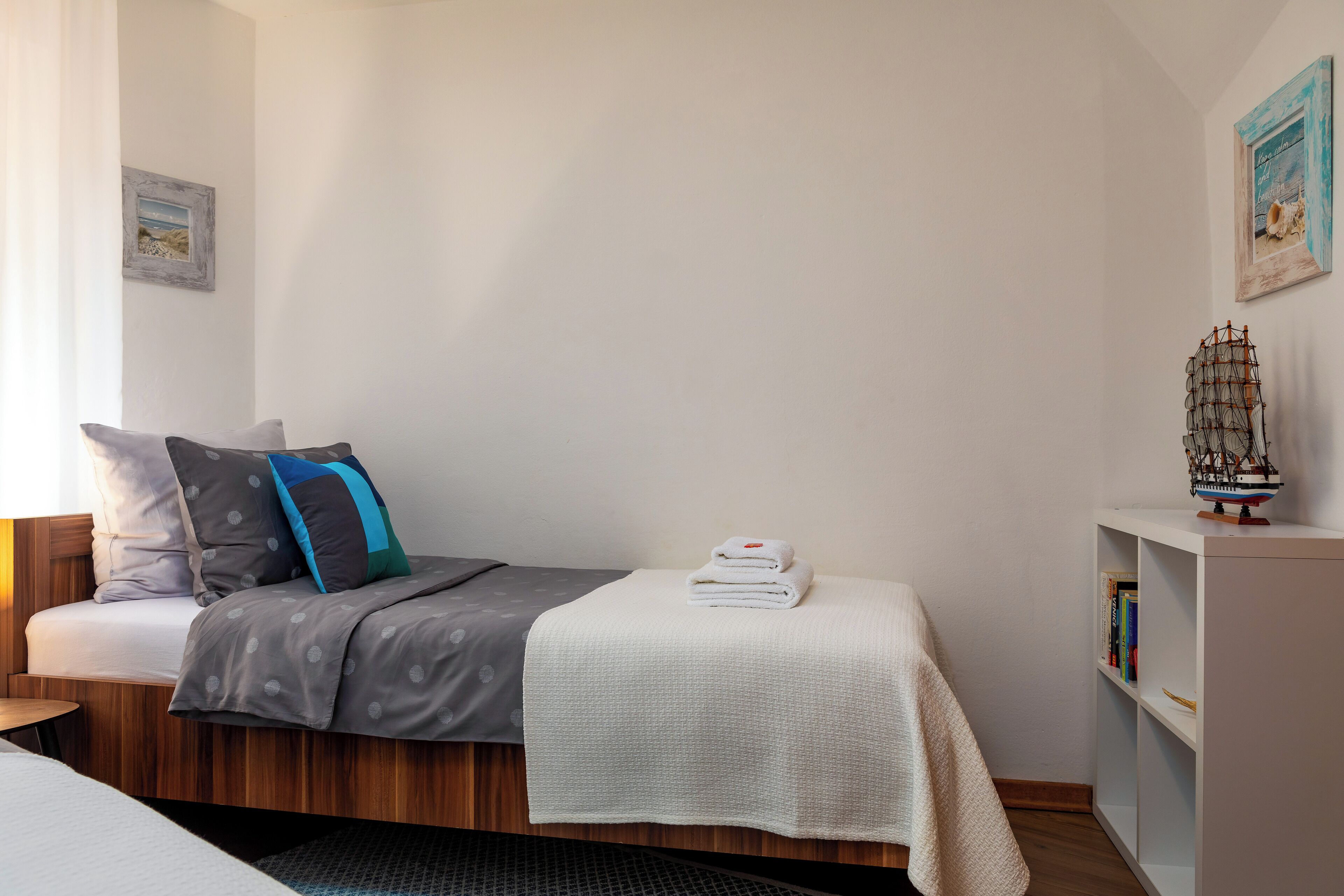 A neatly made bed with a grey and white duvet, pillows, and a folded white towel on a wooden platform.